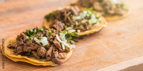 Three pork pastor street tacos in a yellow corn tortilla with beef and onion on a wooden table photo