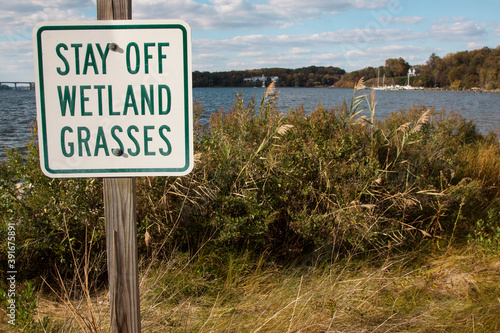 Stay Off Wetland Grasses sign at the grassy edge of blue water.