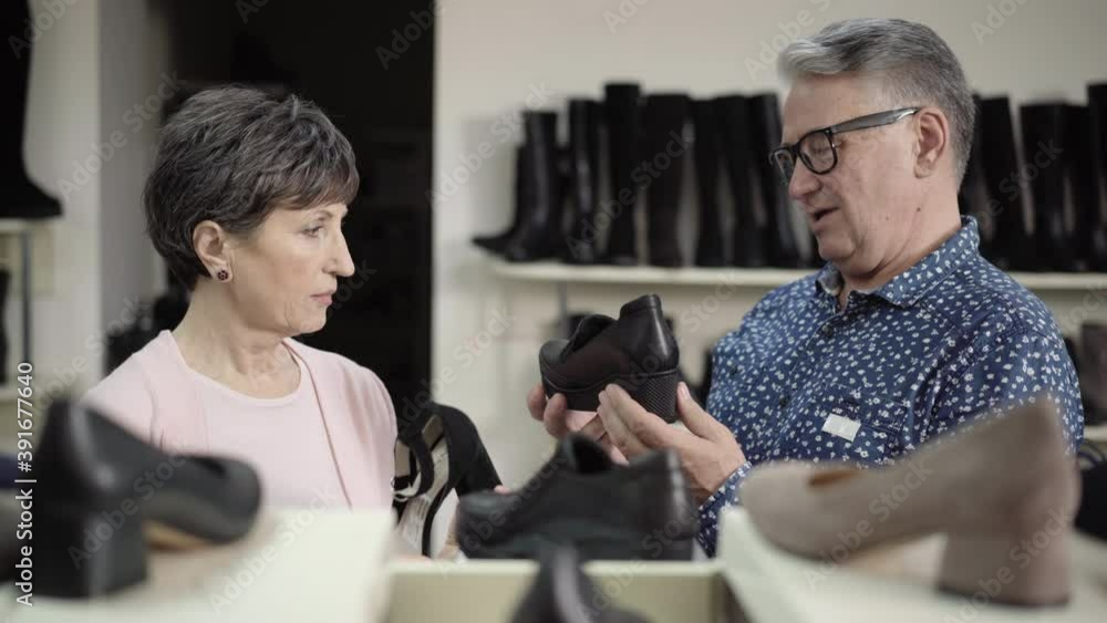 Senior Caucasian husband and wife choosing boots in shoe store. Portrait of handsome man and beautiful woman selecting footwear for elegant lady in shop. Family buying high-heels during sales. Senior Caucasian husband and wife choosing boots in shoe store. Portrait of handsome man and beautiful woman selecting footwear for elegant lady in shop. Family buying high-heels during sales.