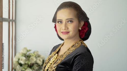 A portrait of a costume traditional Javanese woman in kebaya and paes ageng. Standing by the window photo