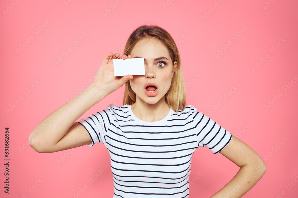 Woman with a business card in her hands a striped T-shirt pink background Copy Space advertising