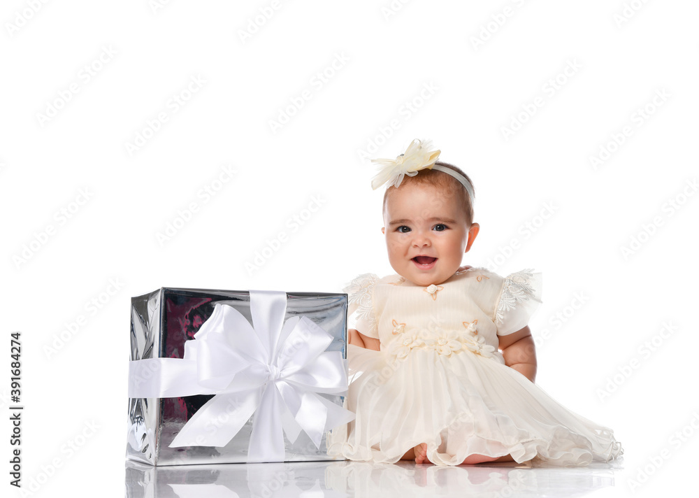 Little baby princess in a smart white dress sits in a white studio with a gift box with a ribbon. Little baby princess in a smart white dress sits in a white studio with a gift box with a ribbon.