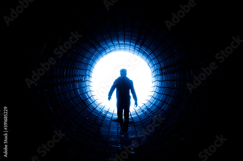 Silhouette of a man walking to the light at the end of a big tunnel. Concept of escape, exit, freedom, clinical death
