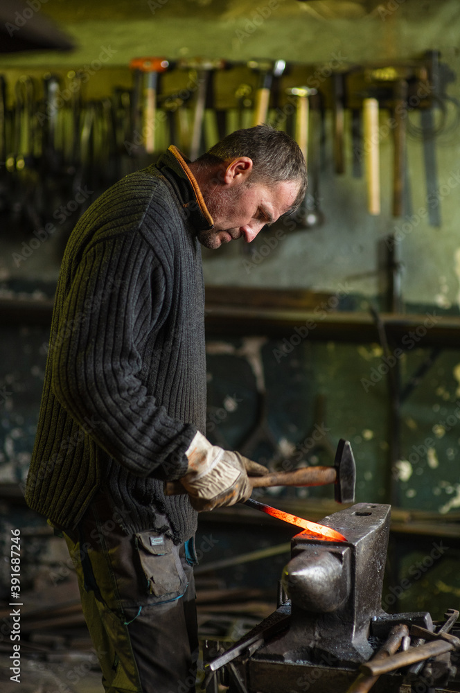 A blacksmith forging a red-hot iron billet on an anvil with a hammer. Handicraft concept A blacksmith forging a red-hot iron billet on an anvil with a hammer. Handicraft concept