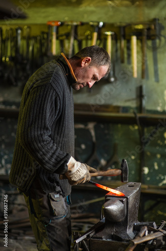 A blacksmith forging a red-hot iron billet on an anvil with a hammer. Handicraft concept