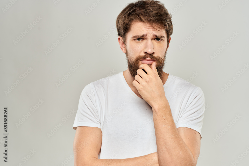 A man in a white t-shirt with a beard emotions displeased facial expression light background A man in a white t-shirt with a beard emotions displeased facial expression light background