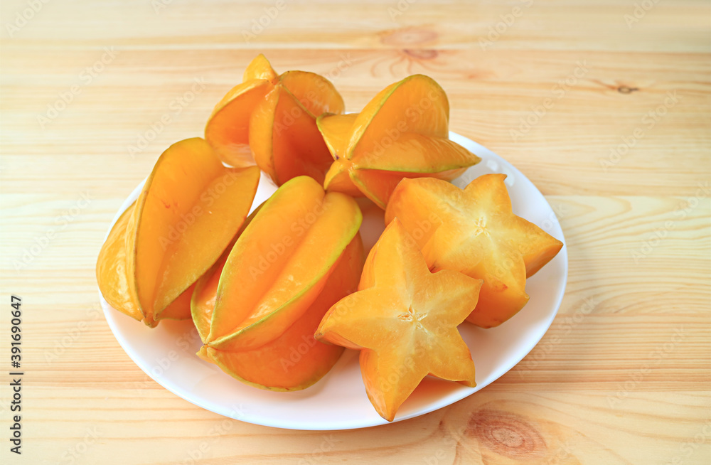 Plate of Juicy Fresh Ripe Starfruit's Cross Sections with Whole Fruit on the Wooden Table Plate of Juicy Fresh Ripe Starfruit's Cross Sections with Whole Fruit on the Wooden Table