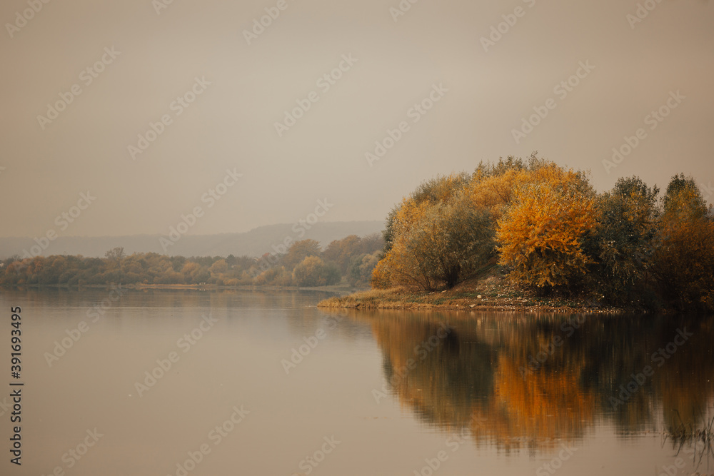 Autumn colourful orange and green foliage of trees over river with reflection in river.
