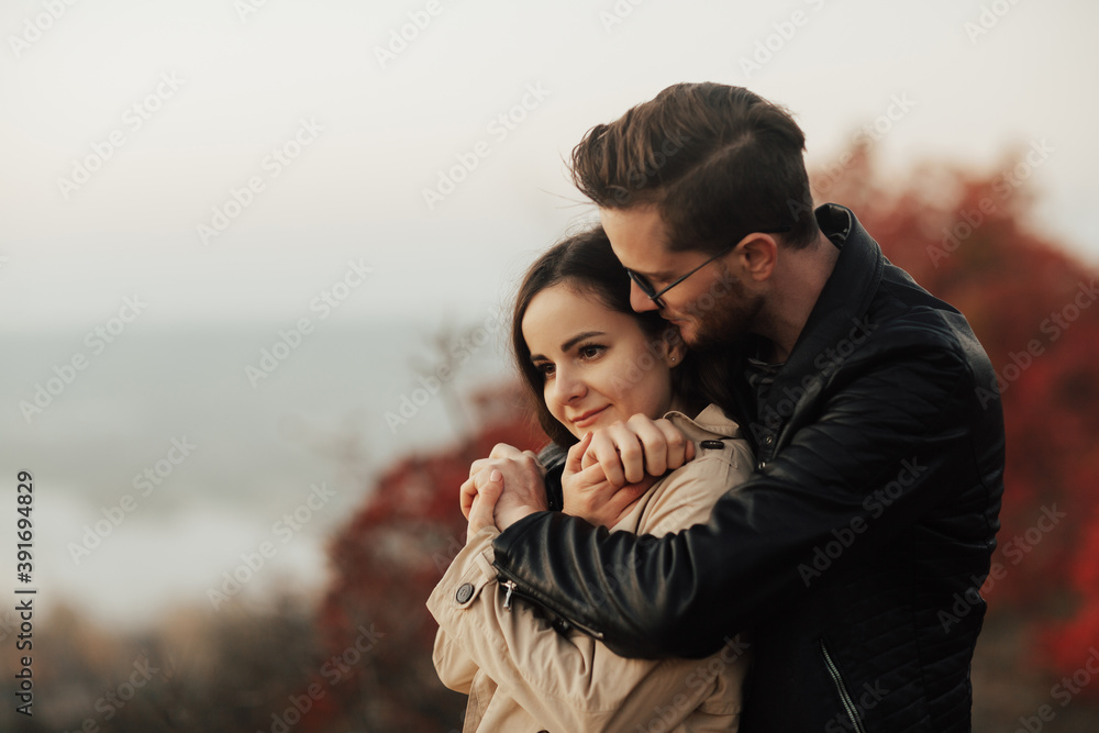 Close up photo of happy couple. Stylish man in eyeglasses is hugging girl from the back. Close-up of hands together.