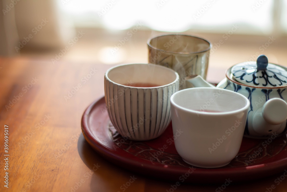 日の当たるテーブルに置かれた急須と入れたてのほうじ茶の入った湯飲み 日の当たるテーブルに置かれた急須と入れたてのほうじ茶の入った湯飲み