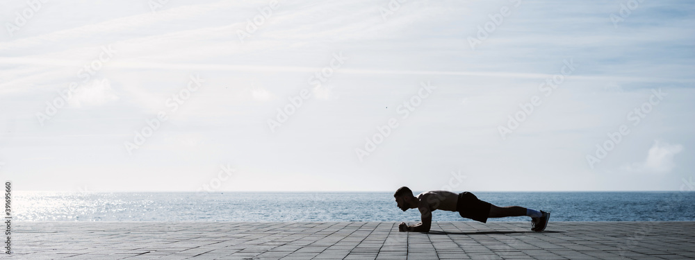 Fit young man doing plank on seafront. Fitness training in morning outdoors. Working out during lockdown outside the gym. - obrazy, fototapety, plakaty 