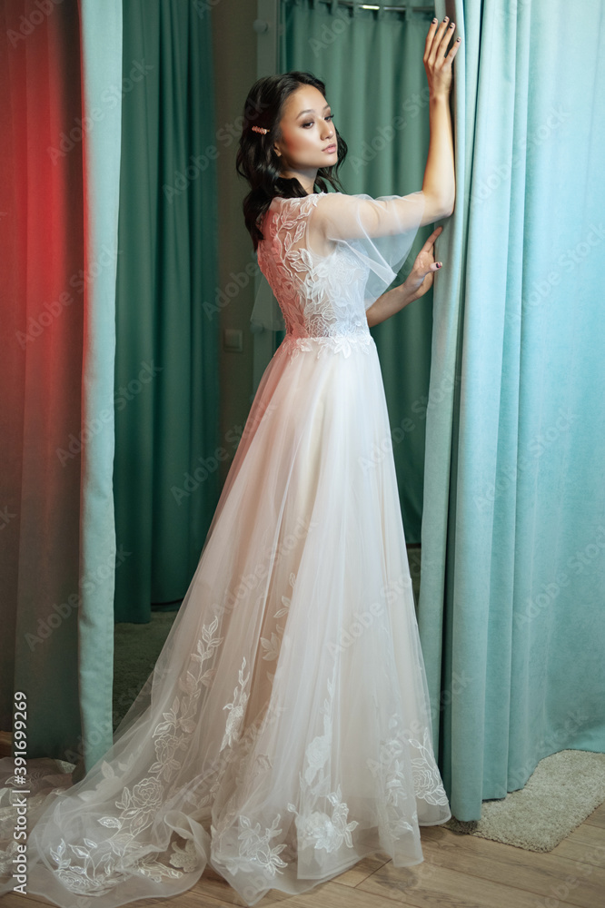 Fototapeta premium Portrait of a young bride in a fashionable wedding dress with beautiful makeup and hairstyle