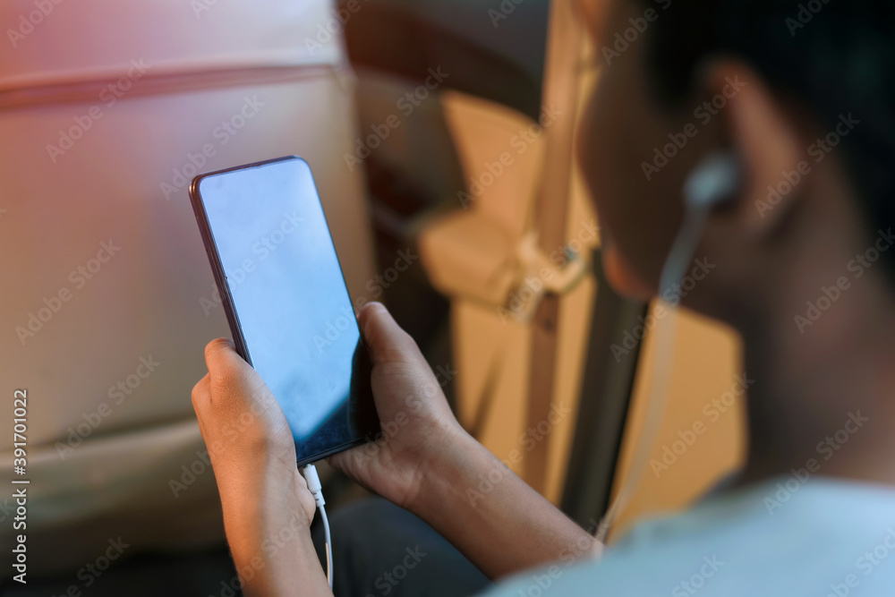 Cute indian child sitting in car and using smart phone and headphones gadget