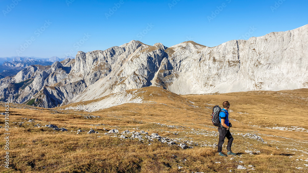A panoramic capture of a man hiking in Hochschwab region in Austrian Alps. The flora overgrowing slopes is turning golden. Autumn vibes in the mountains. Idyllic landscape. Freedom and wilderness