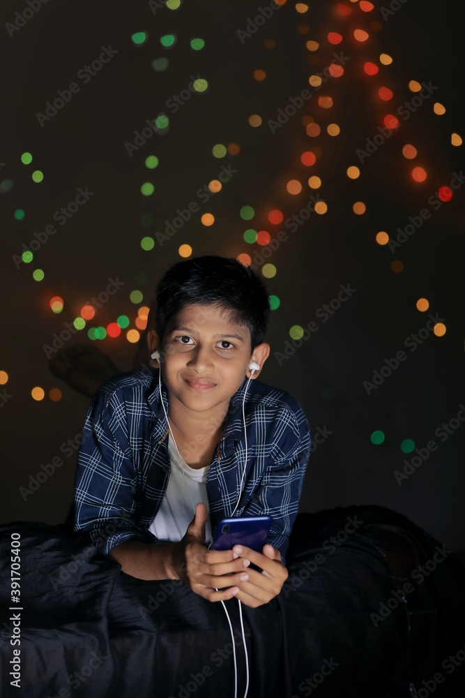 Cute indian child using smart phone and headphones gadget over lighting background Cute indian child using smart phone and headphones gadget over lighting background