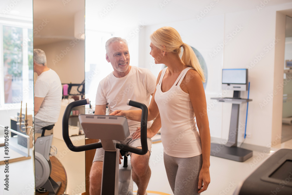 Man on a treadmill talking to his female instructor and smiling Man on a treadmill talking to his female instructor and smiling