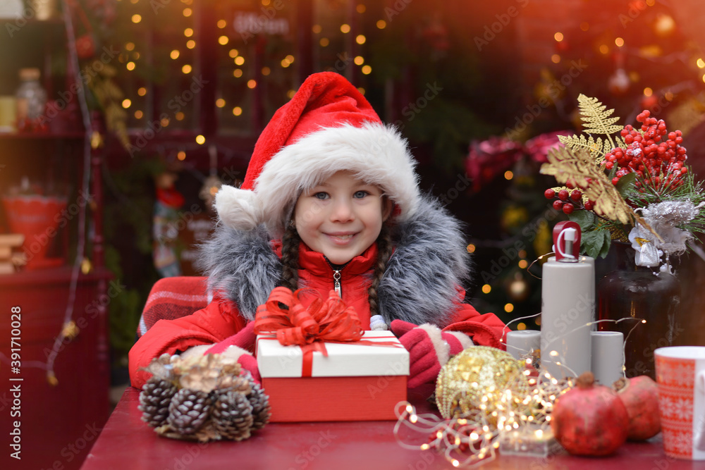 Happy little girl wearing santa hat holding a gift box on the background of the Christmas background ! Happy New Year and Merry Christmas! Happy little girl wearing santa hat holding a gift box on the background of the Christmas background ! Happy New Year and Merry Christmas!