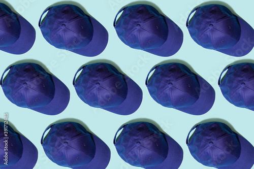Pattern. Copy the image of a blue baseball cap on a light green background. Hats arranged in a row. View from above.
