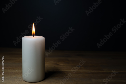A white burning candle on a wooden table, dark background and copy space
