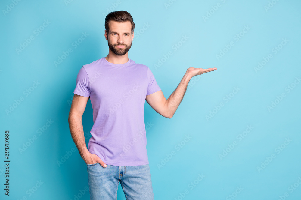 Photo of young attractive man hold hand demonstrate present product advert isolated over blue color background Photo of young attractive man hold hand demonstrate present product advert isolated over blue color background