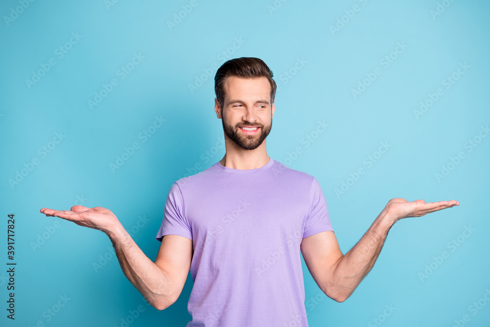 Photo of young handsome guy hold palms balance promo demonstrate product look empty space isolated over blue color background Photo of young handsome guy hold palms balance promo demonstrate product look empty space isolated over blue color background