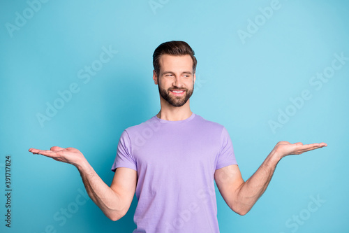 Photo of young handsome guy hold palms balance promo demonstrate product look empty space isolated over blue color background