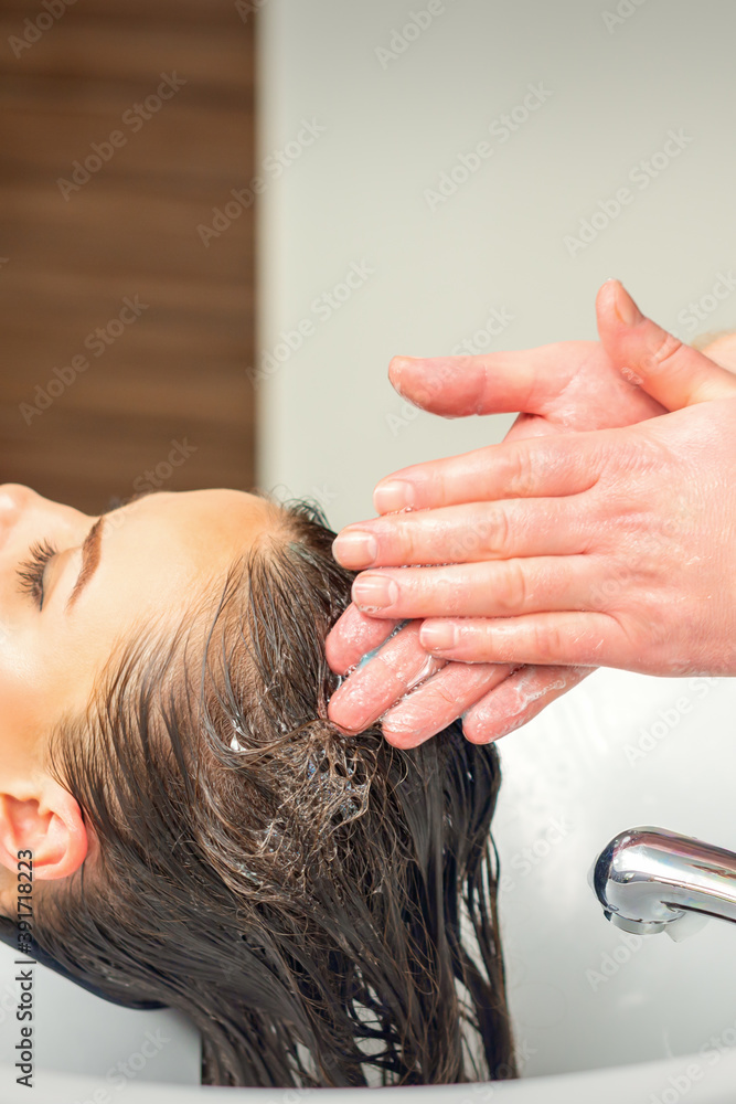 Fototapeta premium Beautiful young woman washing her hair by hands of male hairdresser in hair salon