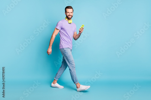 Full length body size photo of hipster wearing casual clothes headphones keeping smartphone isolated on bright blue color background