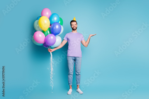 Full length body size photo of happy funny man colorful balloons keeping copyspace on hand smiling isolated on vivid blue color background © deagreez