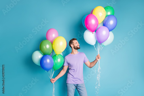 Photo portrait of guy holding helium balloons in two hands isolated on pastel blue colored background
