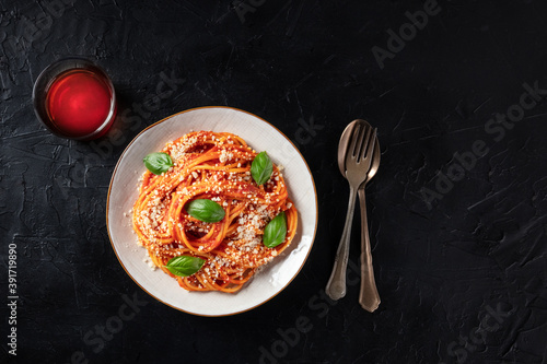 Pasta dish. Spaghetti with tomato sauce, Parmesan cheese and basil leaves, shot from above on a dark table with copy space