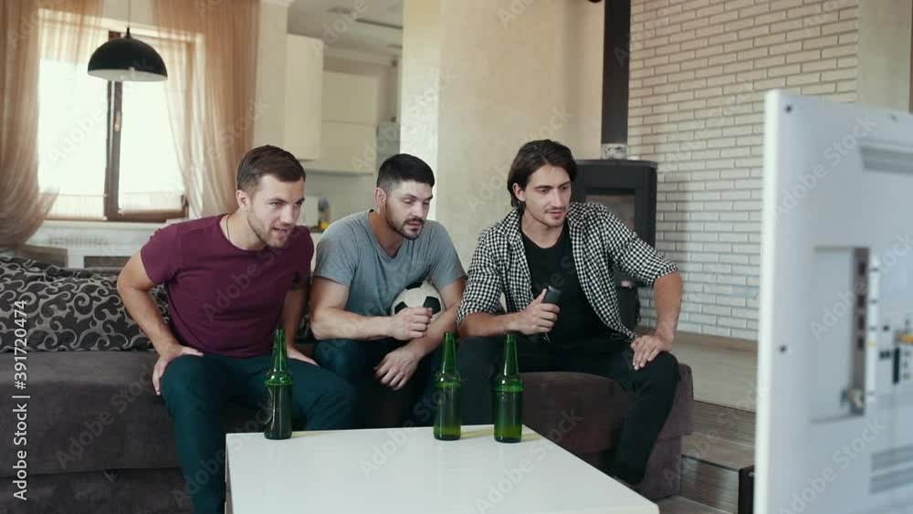Three adult male friends with beer on table watching soccer indoors and celebrating victory. Three adult male friends with beer on table watching soccer indoors and celebrating victory.