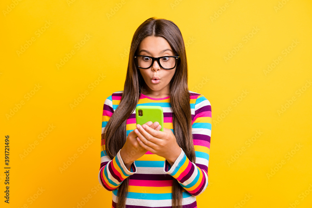 Photo portrait of young schoolgirl with amazed face using smartphone typing staring isolated on vibrant yellow color background Photo portrait of young schoolgirl with amazed face using smartphone typing staring isolated on vibrant yellow color background