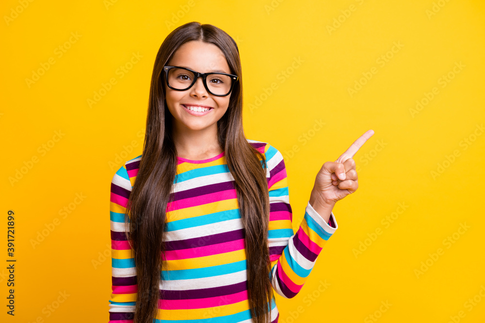 Photo portrait of nice little girl with long brunette hair pointing at empty space with finger isolated on vivid yellow color background