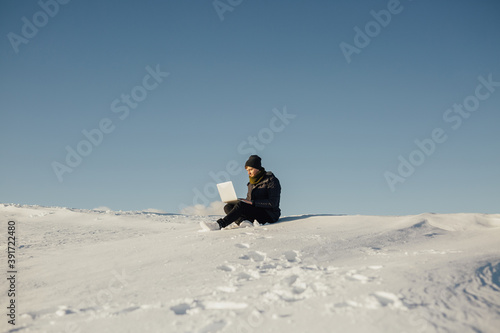 Young tourist using laptop on snowy mountain. White snow and blue sky. Copy space for advertisement. © eduard