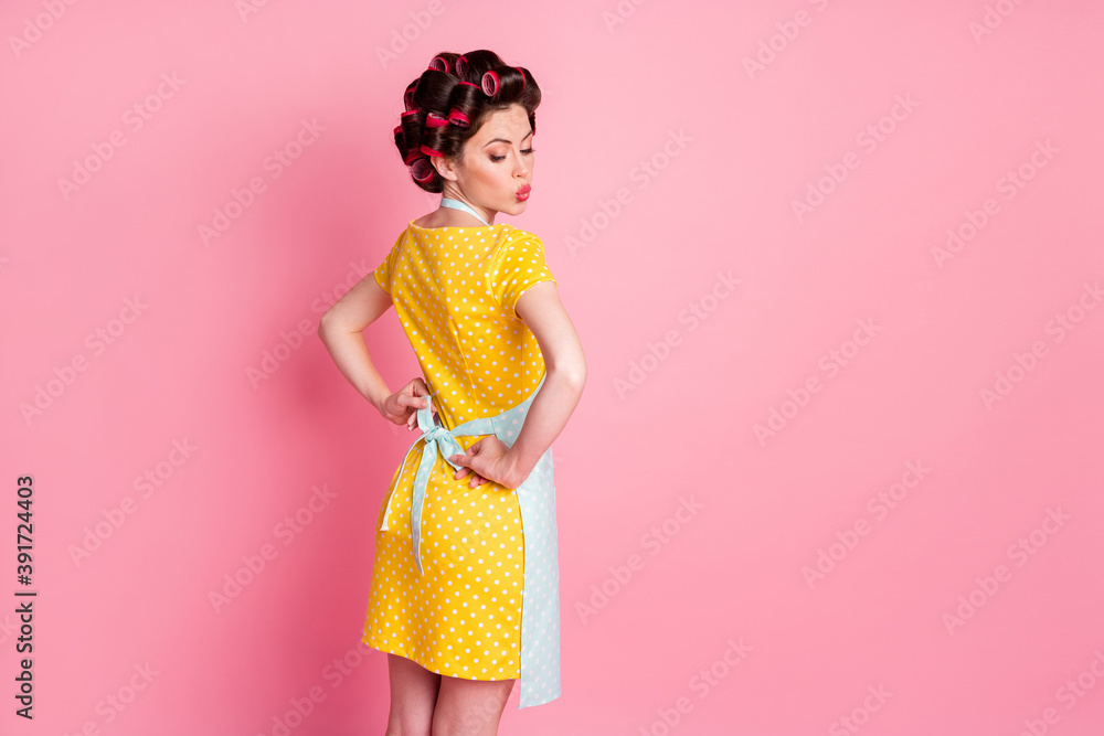 Back rear spine view photo of sweet girl wear apron retro style clothes hair rollers isolated over pink color background
