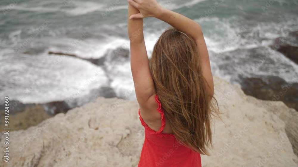 Sexy Girl In Cocktail Red Dress Standing On The Rocks And Watching The Sea Waves With Hands On Head - Eastern Suburbs, NSW, Australia. - high angle shot