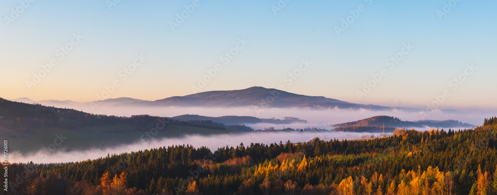 misty landscape at sunset, mountains rising from clouds of fog in the background, clear sky - mountain Klet, Czech republic