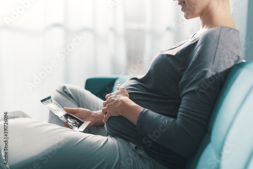 Pregnant woman sitting on the sofa and watching ultrasound images of her baby photo