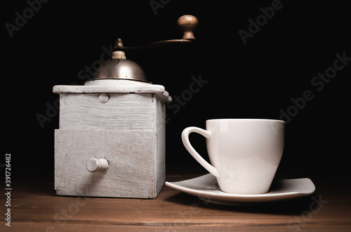 Vintage retro manual grinder and a small cup of coffee on a wooden table, with black background.
