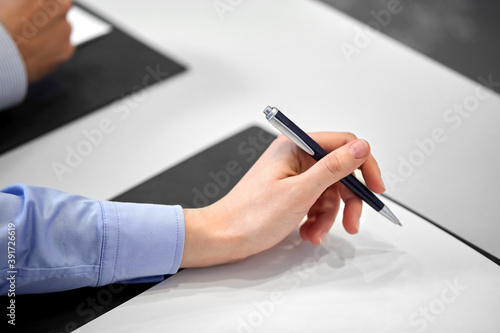 people, business and corporate concept - close up of businesswoman with pen and paper at office
