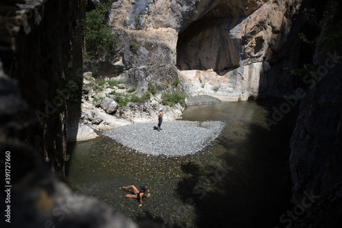 Photo from a stone bridge,of a woman who lie down inside the cold water of Venetikos river.A man admires the high cliffs of 200 meters of the magnificent Gorge.