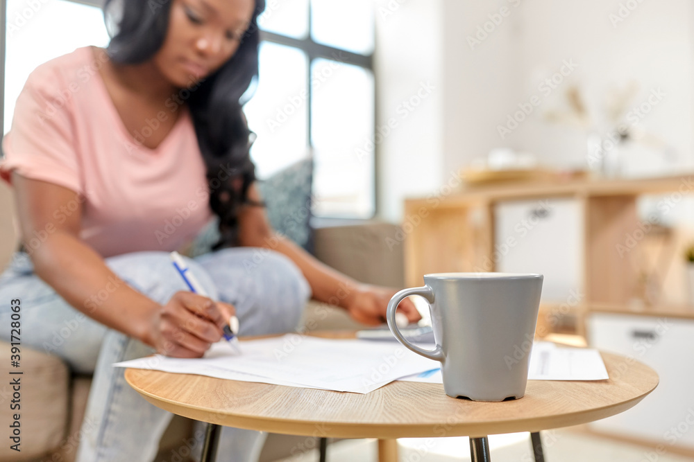 accounting, taxes and finances concept - cup of coffee on table and young african american woman with papers and calculator at home accounting, taxes and finances concept - cup of coffee on table and young african american woman with papers and calculator at home
