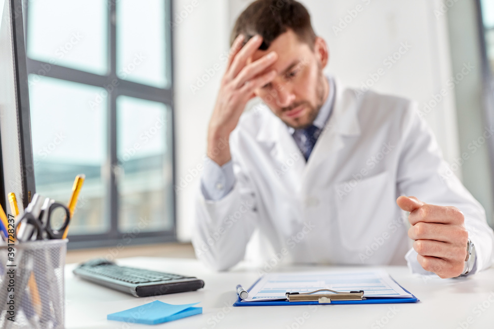 healthcare, medicine and people concept - stressed male doctor with clipboard at hospital healthcare, medicine and people concept - stressed male doctor with clipboard at hospital