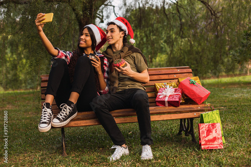 Couple in love shares Christmas gifts - Young couple at Christmas time - Couple takes a picture on the park bench.