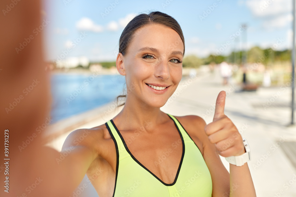 people, sport and fitness concept - portrait of smiling young sporty woman taking selfie picture and showing thumbs up outdoors on sea promenade people, sport and fitness concept - portrait of smiling young sporty woman taking selfie picture and showing thumbs up outdoors on sea promenade