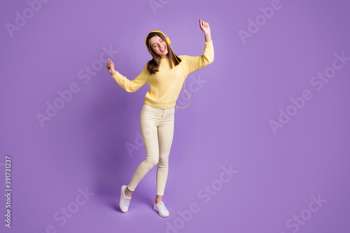 Full length body size photo of dreamy girl listening to music with earphones dancing singing isolated on vibrant violet color background