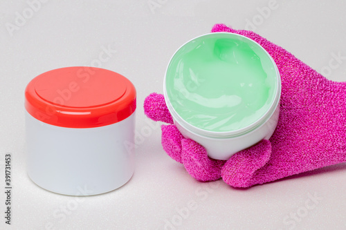 Close-up of a closed and an open container with cooling gel (horse balm) for sports injuries on a light background. The open container is held by a pink massage glove. Copy space. Macro. photo