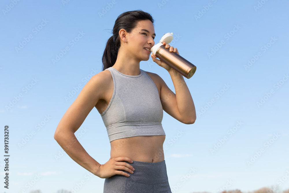 Young Vietnamese-American woman drinks water from water bottle outside after yoga
