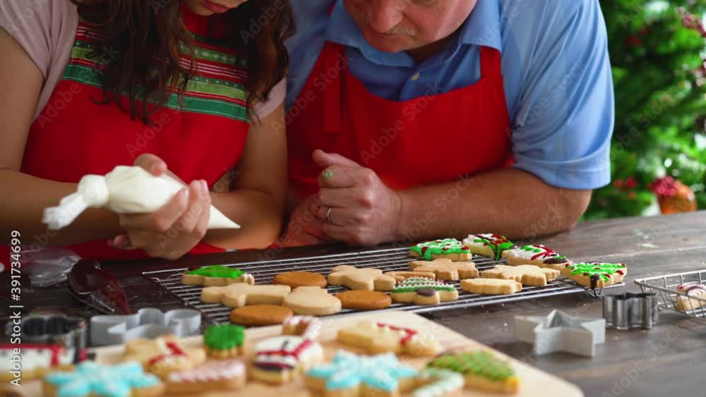 Senior father and teen daughter making cookies together with Christmas tree in background. Happy family celebrating in santa hat at home Senior father and teen daughter making cookies together with Christmas tree in background. Happy family celebrating in santa hat at home